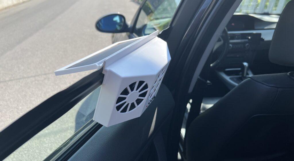 Bilde av en hvit solcelledrevet vifte som henger i et bilvindu. Vi har testet denne solcelledrevne viften til bilen for å finne ut om det er verdt pengene.