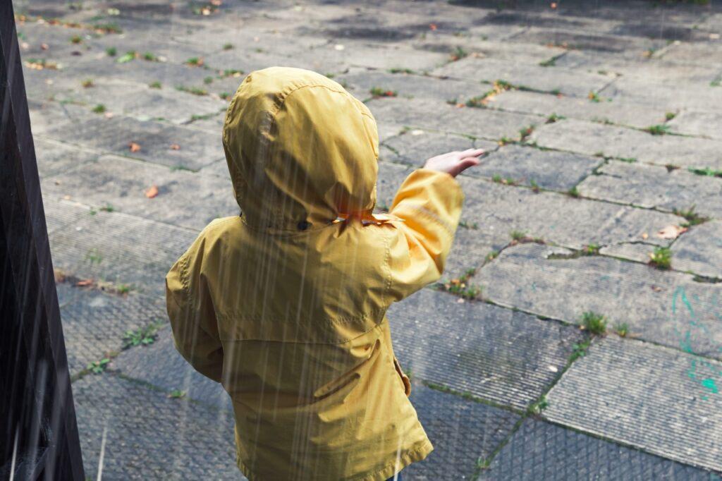 Barn i gul regnjakke står med ryggen til og holder hånden ut for å kjenne på regnet. Ute regner det kraftig. Få regntøyet til å vare i lang tid ved å vaske det riktig, samt impregnere det når det trengs. Vi forklarer hvordan.