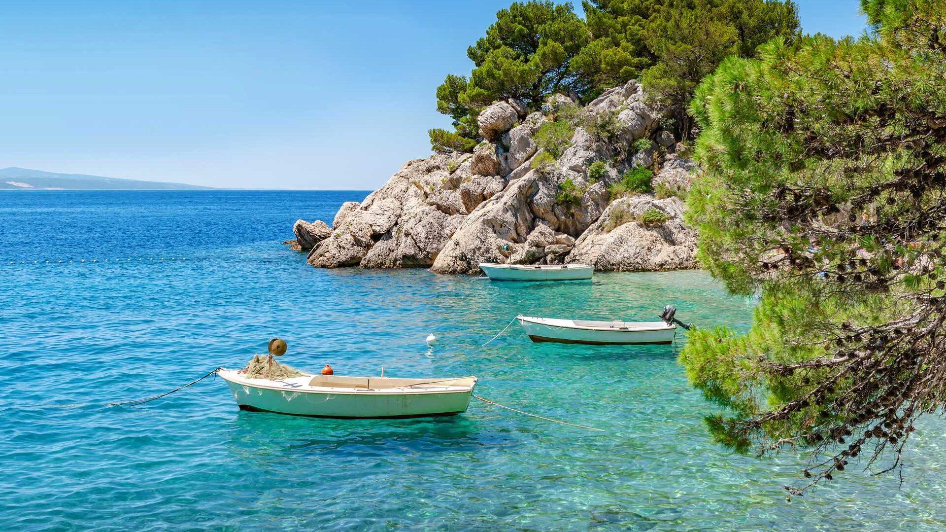 På bilde ser du et krystallklart hav utenfor kysten av feriefavoritten Kroatia. På bilde ser vi flott natur og 3 båter som flyter i havet. Nå kan du sikre deg billig sommerferie til Kroatia.