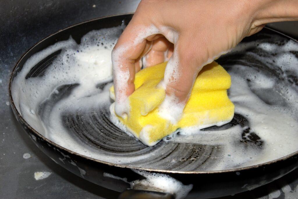 Stekepanne i karbonstål: Person vasker en stekepanne med såpe og svamp.