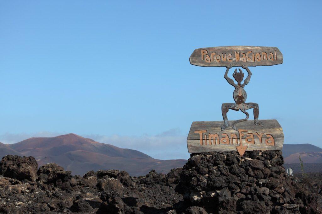 Bilde av en figur som holder et skilt hvor det står Timanfaya som er en nasjonalpark på Lanzarote. Vi har snakket med redaktør i Lanzaroteposten, Ola Kjeldstad som gir oss sine beste tips til en topp 5 Lanzarote-guide.