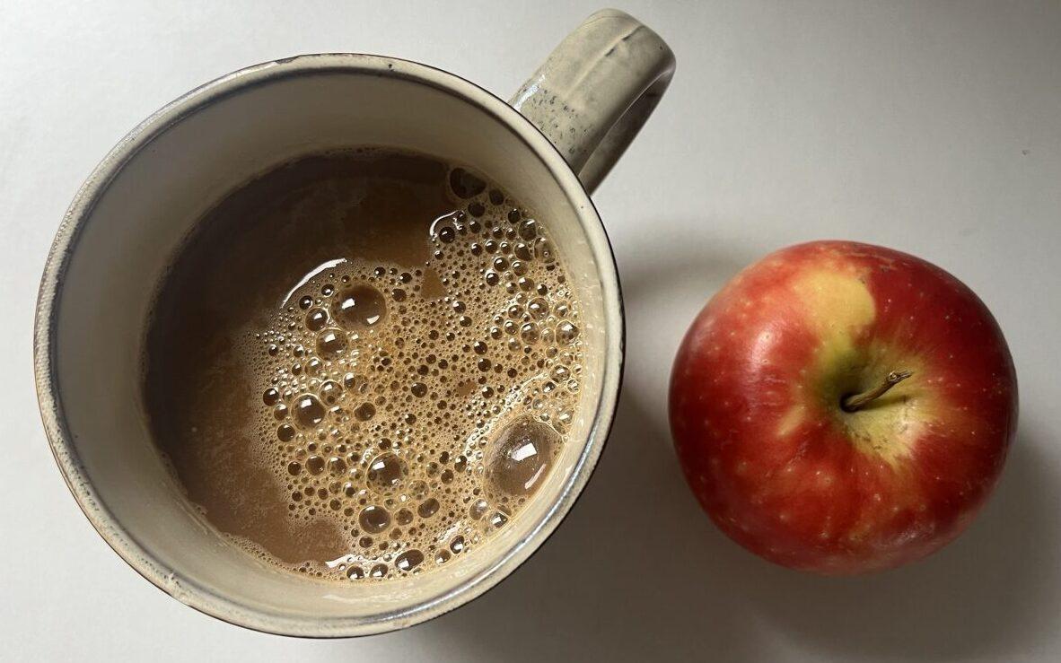 Bilde av en beige keramikk-kopp med sort kaffe på marmorbord ved siden at et eple. Vi forteller om overraskende forskning som tilsier at det ikke er lurt å drikke kaffe til maten og hvorfor!