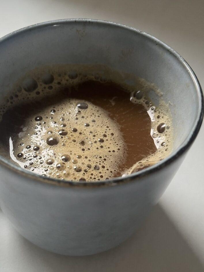Bilde av en blå keramikk-kopp med sort kaffe på marmorbord. Vi forteller om overraskende forskning som tilsier at det ikke er lurt å drikke kaffe om morgenen og hvorfor!
