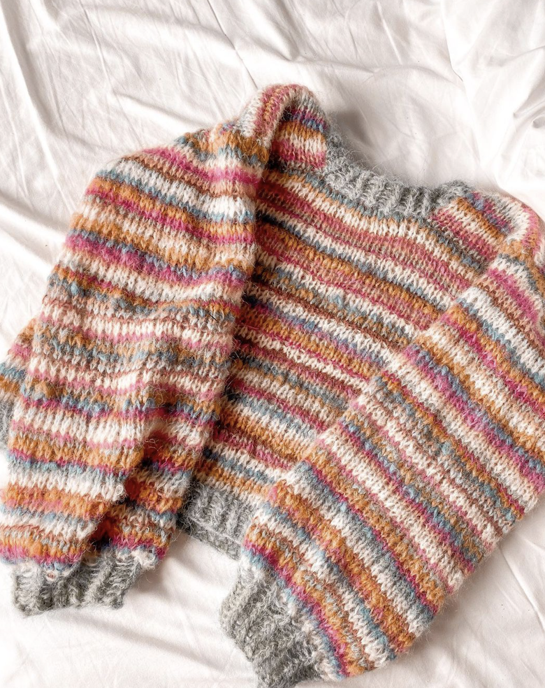 bilde av strikket genser til dame. Den ligger på senga og har masse farger. Perfekt gratis strikkeoppskrift til restegarn. Den har fargen rød, grønn, grå og hvit. Nybegynner og gratis.