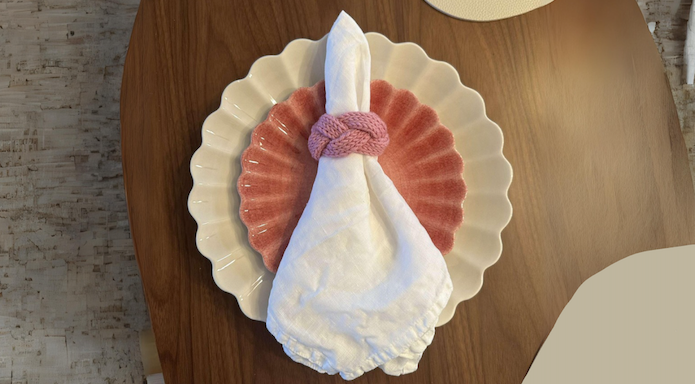 Strikkeoppskrift gratis på serviettring. Rosa serviettring, ligger på en tallerken.