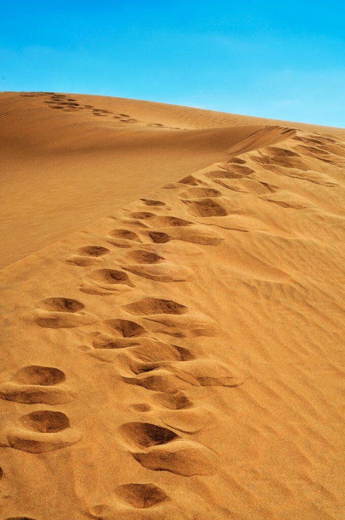 Gylden sand på en sanddyne i Maspalomas på Gran Canaria. I sanden ser mat fotspor og bak sanddynen ser man knallblå himmel.