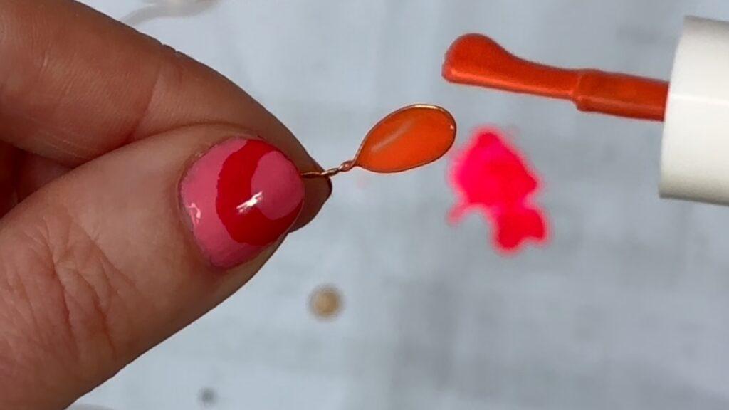 Hånd som lakker orange neglelakk på en løkke av metalltråd.